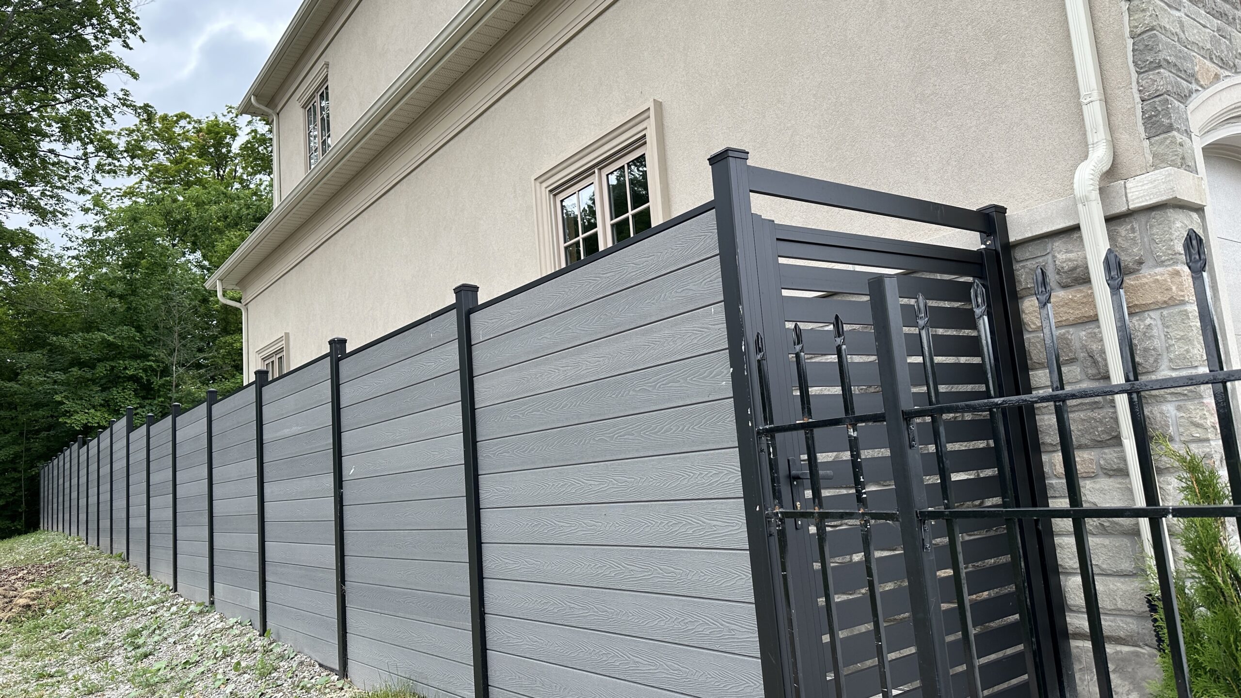 Modern gray fence with vertical panels and a metal gate in front of a building. Modern gray fence with vertical panels and a metal gate in front of a building.