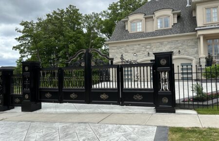 Elegant black wrought iron gate with gold accents in front of a stone mansion.