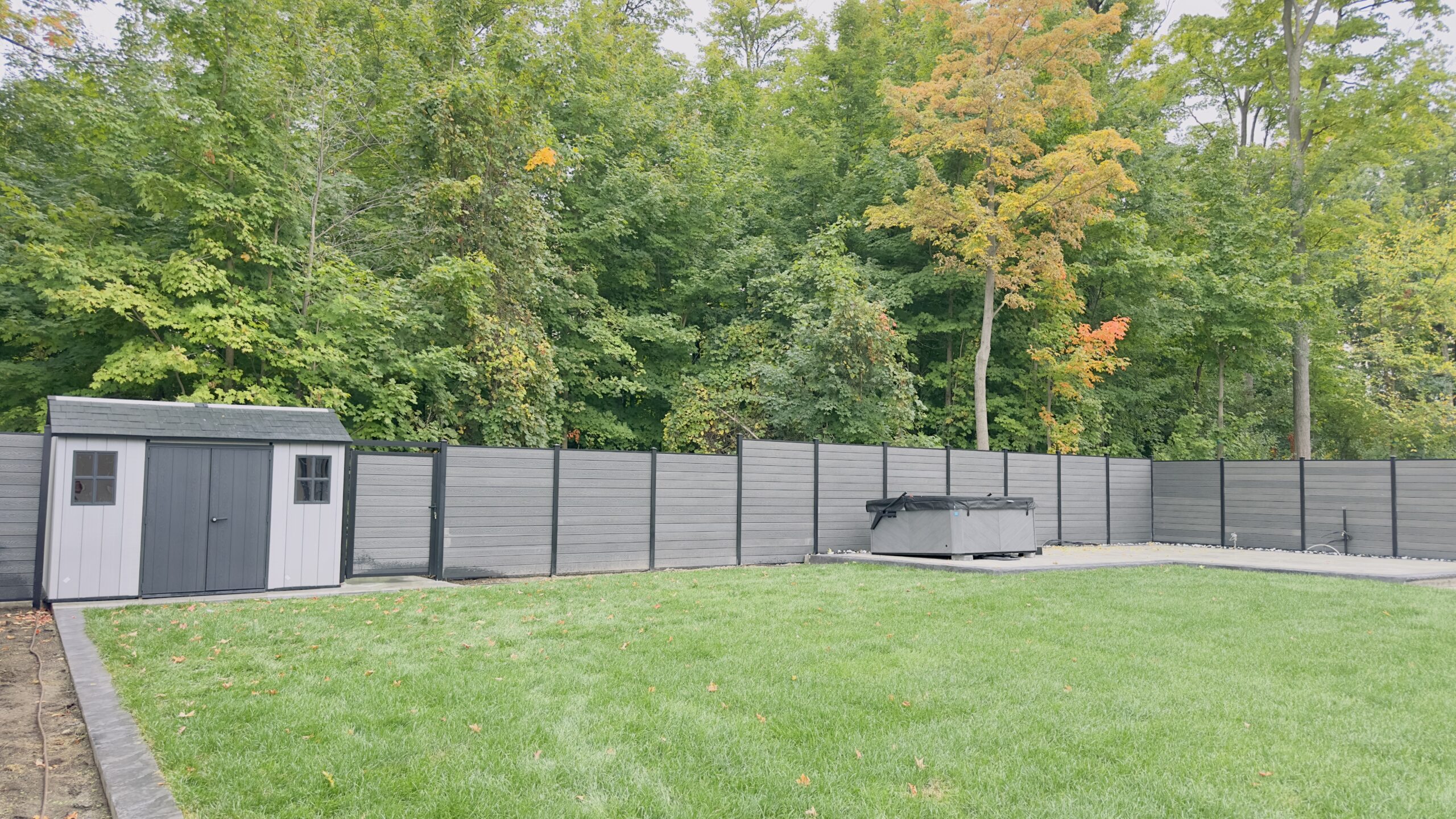 A modern black fence surrounds a green backyard with trees. A modern black fence surrounds a green backyard with trees.