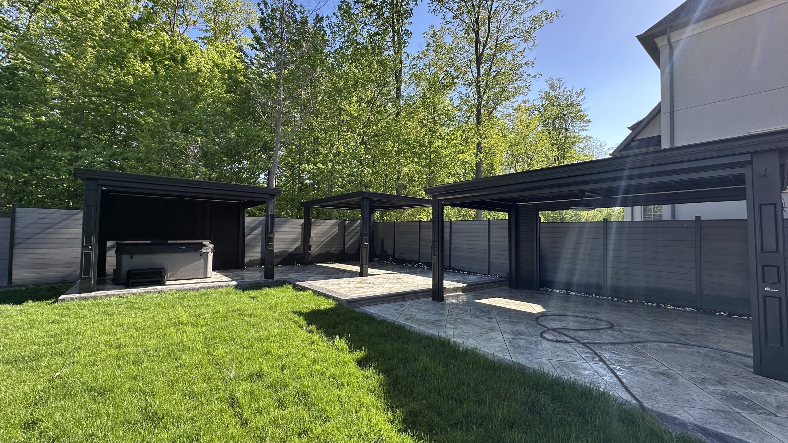 Modern outdoor patio area with pergolas and green lawn under a clear sky. Modern outdoor patio area with pergolas and green lawn under a clear sky.