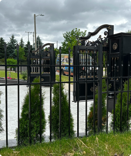 Black metal fence with ornate gates around a green park area on a cloudy day.