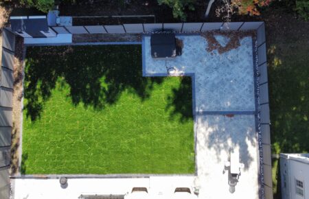 Aerial view of a green lawn beside a paved patio area with shadows.