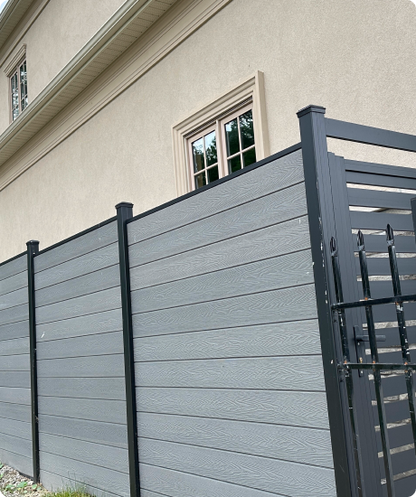 Modern grey fence with a gate alongside a beige building.